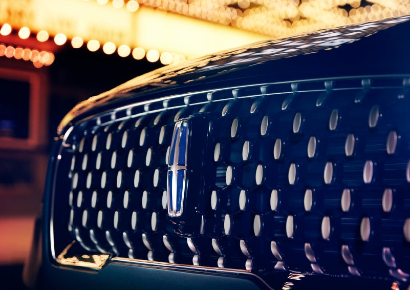 The Corsair Grand Touring grille shows floating chrome ovals that catch the glowing light of a theater marquee and frame the distinctive Lincoln Star | Fair Oaks Lincoln in Naperville IL