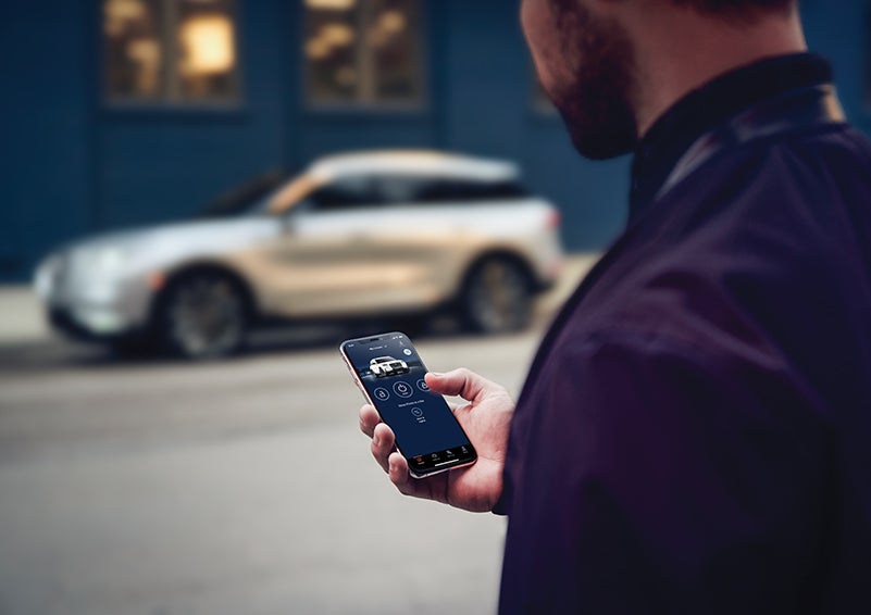 A person is shown interacting with a smartphone to connect to a Lincoln vehicle across the street. | Fair Oaks Lincoln in Naperville IL