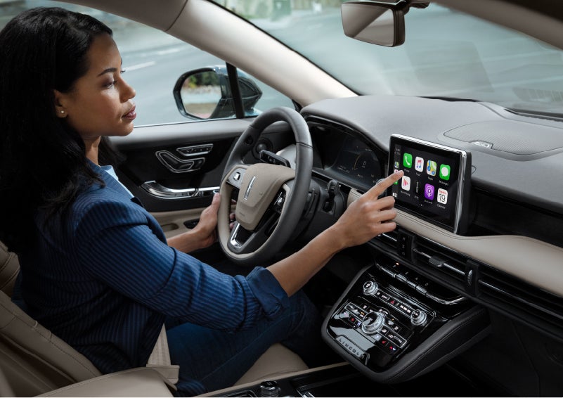 A woman in the driver’s seat of a 2022 Lincoln Corsair is touching the center digital screen to connect to Apple CarPlay<sup>®</sup> | Fair Oaks Lincoln in Naperville IL