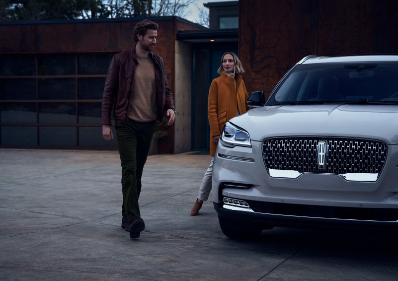 A man and a woman approaching a 2024 Lincoln Aviator® SUV, which illuminates certain lights when they are close | Fair Oaks Lincoln in Naperville IL