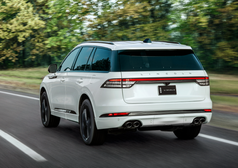 A white 2025 Lincoln Aviator® SUV is being driven away down a road lined with colorful trees. | Fair Oaks Lincoln in Naperville IL