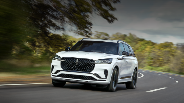 A white 2025 Lincoln Aviator® SUV is being driven down a road lined with trees. | Fair Oaks Lincoln in Naperville IL