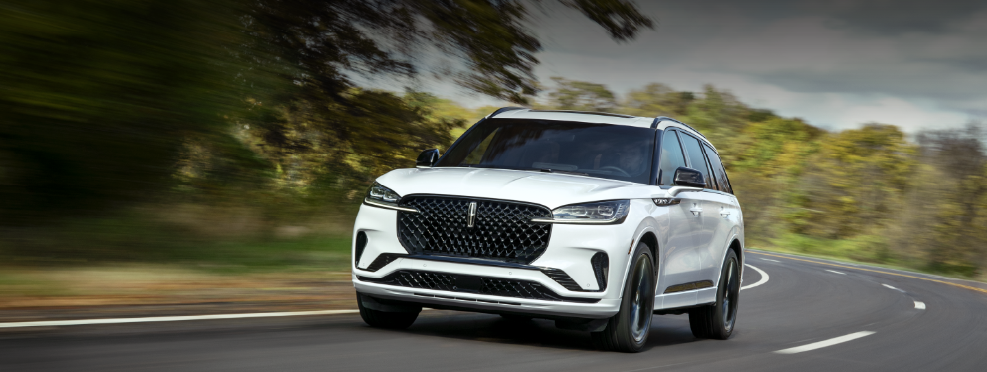 A white 2025 Lincoln Aviator® SUV is being driven down a road lined with trees. | Fair Oaks Lincoln in Naperville IL