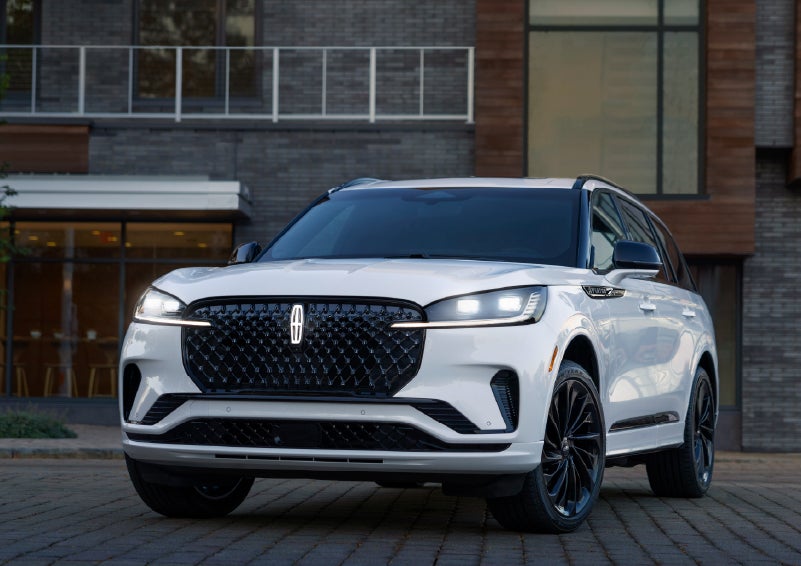 A 2026 Lincoln Aviator® Reserve model is shown with the available Jet Appearance Package parked near a restaurant. | Fair Oaks Lincoln in Naperville IL