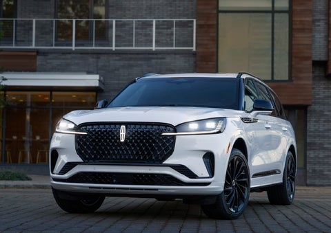 A 2026 Lincoln Aviator® Reserve model is shown with the available Jet Appearance Package parked near a restaurant. | Fair Oaks Lincoln in Naperville IL