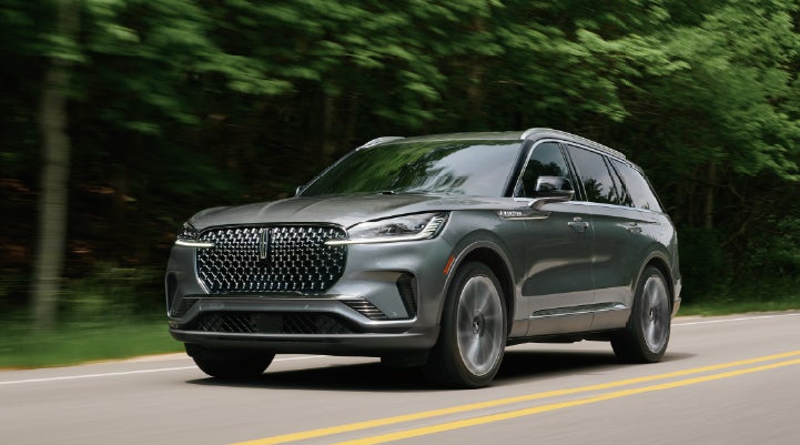 A 2027 Lincoln Aviator® SUV is being driven down a road lined with trees. | Fair Oaks Lincoln in Naperville IL